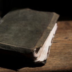 Leather covered old bible lying on a wooden table in a beam of sunlight (not an isolated image) Shallow Depth of field – Focus on closest edge of bible
